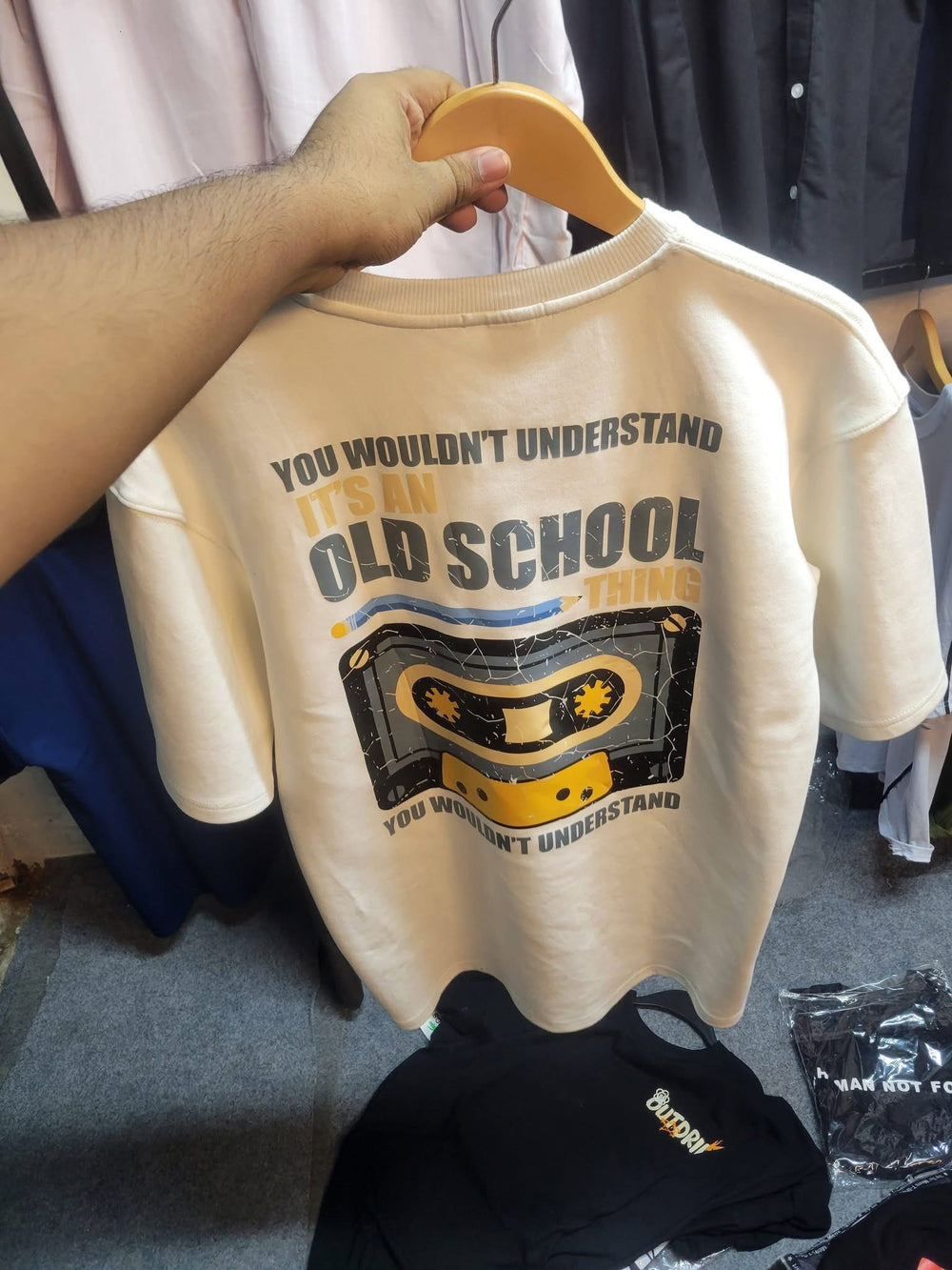 A cream graphic T-shirt held on a wooden hanger